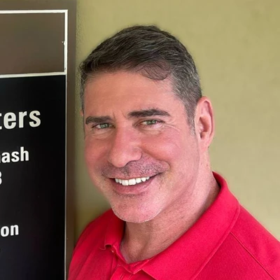 Headshot photo of Dr. Nelson Bulmash wearing a red collared shirt and smiling outside of his office